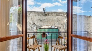 A balcony with two wooden chairs, a potted plant, and a view of a stone wall and green gate. - GuestHost - Cozy 43 sqm ground floor apartment, perfect for three people (accessible via a few steps).The property enjoys a prime location, directly on the beach, with convenient access to the sea. The Taormina - Giardini train station is less than a 10- (Naxos)