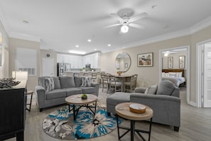 A modern living room with a grey sofa, a coffee table, and a dining area with chairs. - 1521 Crow Creek Golf and Beach Getaway (Calabash)