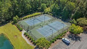 An aerial view of a tennis court complex surrounded by trees and a small pond. - Crow Creek Condo With a Golf Course View 25014 (Calabash)