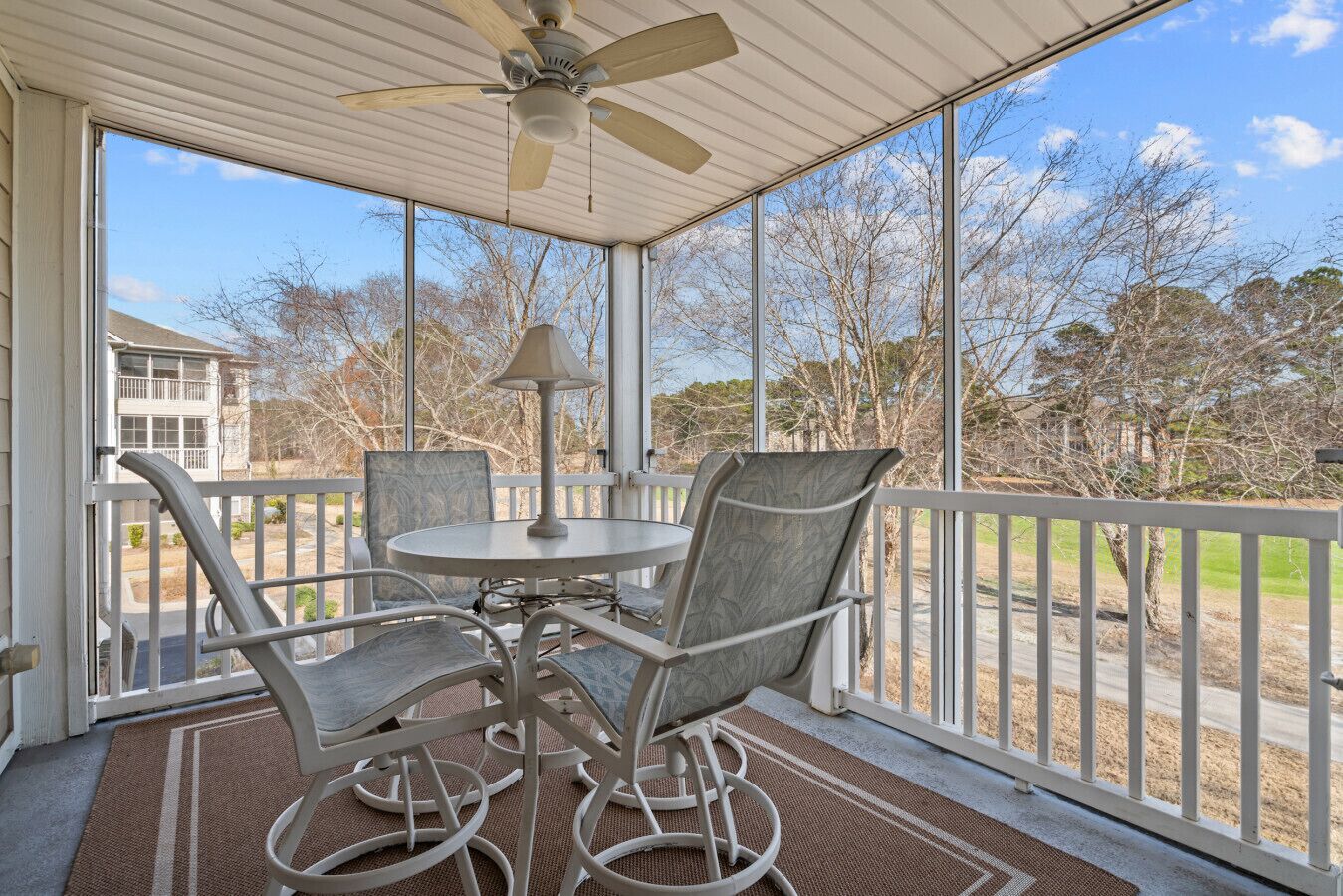 A covered patio with a table and chairs, a ceiling fan, and a view of a residential area.