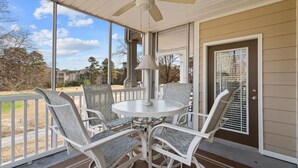 A covered patio with a round table and four chairs, a ceiling fan, and a view of a residential area. - Crow Creek Condo With a Golf Course View 25014 (Calabash)