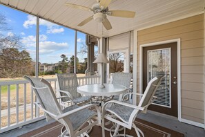A covered patio with a round table and four chairs, a ceiling fan, and a view of a residential area. - Crow Creek Condo With a Golf Course View 25014 (Calabash)