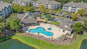 A residential area with a large swimming pool surrounded by lounge chairs and a small pond. - Crow Creek Condo With a Golf Course View 25014 (Calabash)