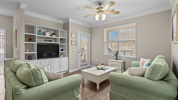 A living room with a television, shelving, and two green armchairs. - Crow Creek Condo With a Golf Course View 25014 (Calabash)