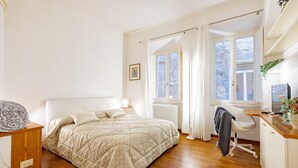 Un dormitorio con cama, mesita de noche, silla, escritorio y ventana.