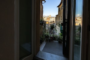 A balcony with a view of a cityscape, a metal railing, and potted plants.