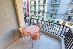 A balcony with a round table and four chairs, overlooking a street with multi-story buildings. - Vibrant Family Apartment for 7 with Balcony Bugibba (St Paul's Bay)
