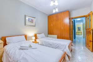 A hotel room with two beds, wooden wardrobe, framed picture on the wall, and a hallway leading to another room. - Vibrant Family Apartment for 7 with Balcony Bugibba (St Paul's Bay)