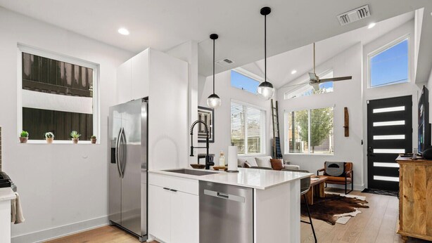 Una cocina moderna con una isla central, electrodomésticos de acero inoxidable, iluminación colgante y un comedor con mesa y sillas de madera.