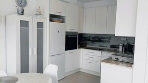 A modern kitchen with white cabinets, a built-in oven, and a dining area with a round table and chairs. - To María Bazarra's house. Sea views, elevator and air conditioning. (A Pobra do Caramiñal)