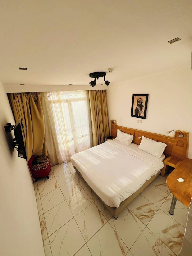 A hotel room with a large bed, a wooden headboard, a bedside table, a TV mounted on the wall, and a small red chair.