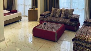 A modern hotel room with a bed, a sofa set, a small table, and a ceiling light fixture. - El Djanoub Hotel (Ghardaia)