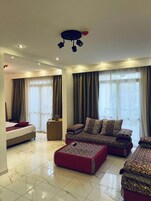 A modern hotel room with a bed, a sofa set, a small table, and a ceiling light fixture.