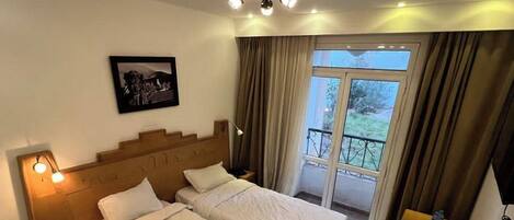 A hotel room with two beds, a large window with a view, a ceiling fan, and a small table with a lamp.