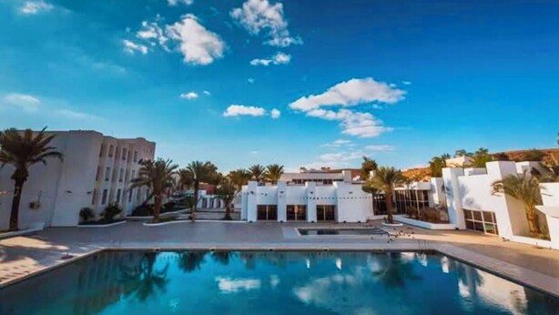 A swimming pool area with a clear blue sky and white buildings. - El Djanoub Hotel (Ghardaia)