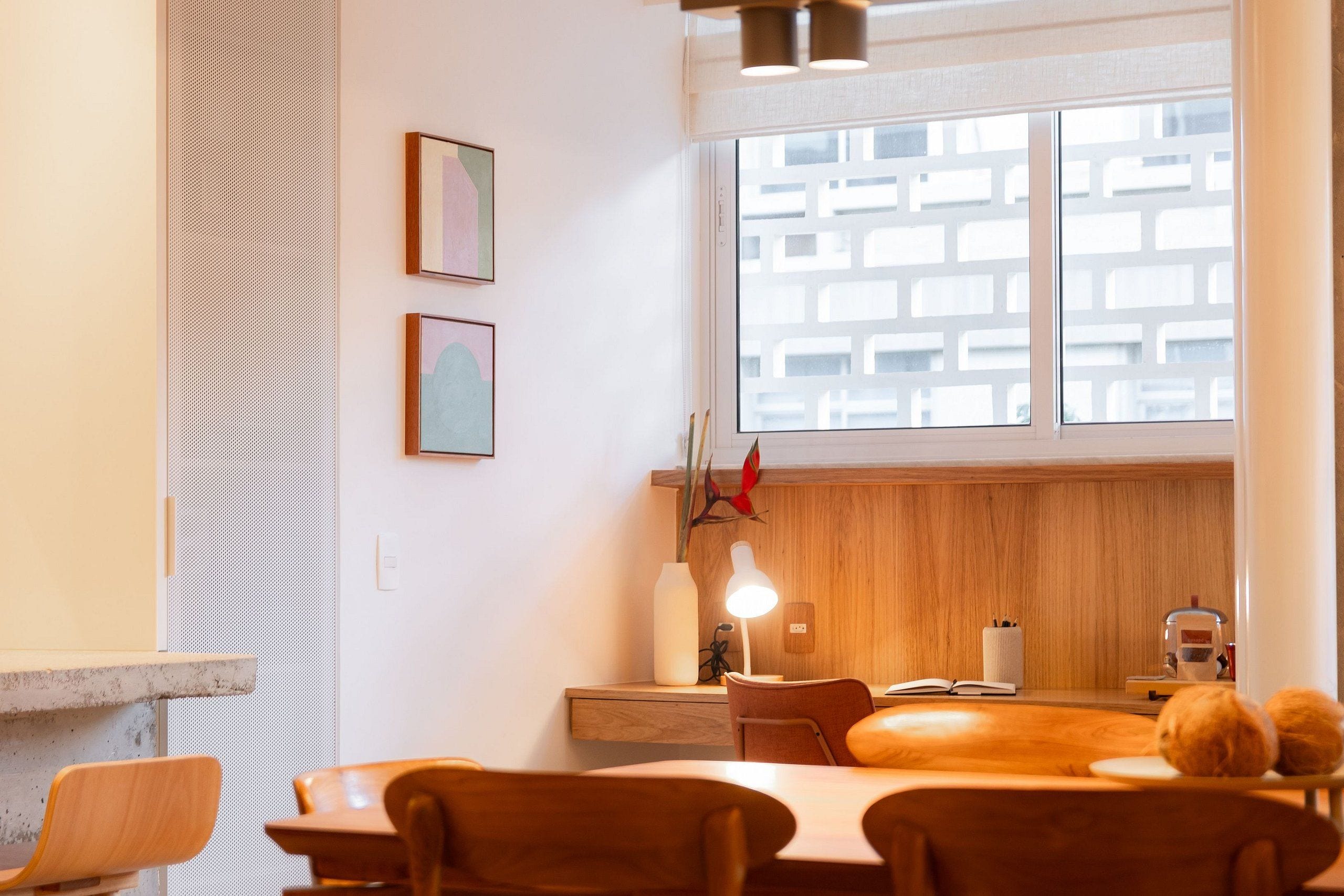 Un comedor moderno con mobiliario de madera, un ventanal con vistas a edificios y dos obras de arte enmarcadas en la pared.