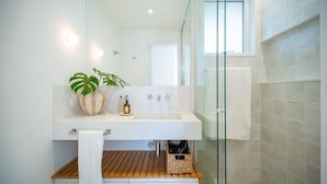 Un baño moderno con lavamanos blanco, tocador de madera y cabina de ducha de vidrio.