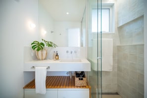 A modern bathroom with a white sink, wooden vanity, and a glass shower enclosure. - Leblon | 3 Quartos, 2 min da Praia - por Casapē Rio (Rio de Janeiro)