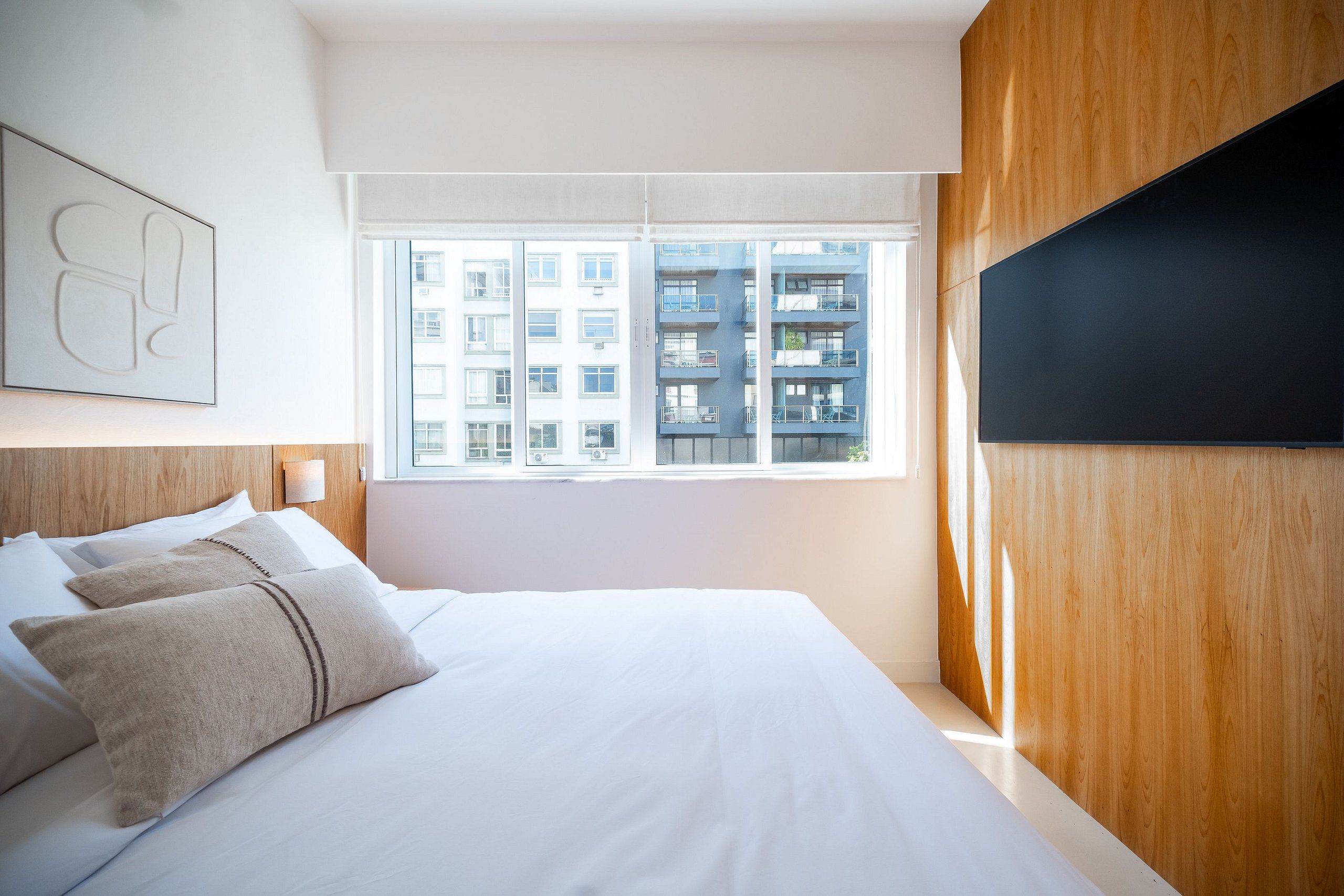 Ein modernes Hotelzimmer mit einem großen Bett, Holzvertäfelung, einem Flachbildfernseher und Blick auf ein Gebäude durch das Fenster.