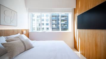 Une chambre d’hôtel moderne avec un grand lit, des panneaux de bois, un téléviseur à écran plat et une vue sur un immeuble par la fenêtre.
