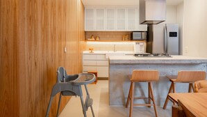 Una cocina moderna con gabinetes de madera, microondas integrado, refrigerador de acero inoxidable e isla de concreto con taburetes de bar.