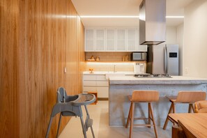 A modern kitchen with wooden cabinets, a built-in microwave, a stainless steel refrigerator, and a concrete island with bar stools. - Leblon | 3 Quartos, 2 min da Praia - por Casapē Rio (Rio de Janeiro)