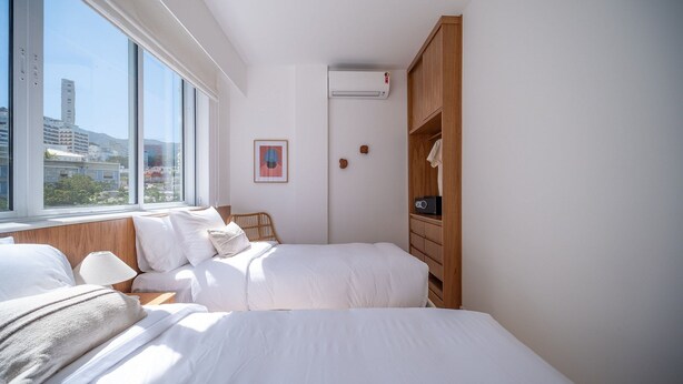 Habitación de hotel con dos camas, un armario de madera, un equipo de aire acondicionado y una ventana con vista a la ciudad.