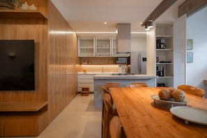 A modern kitchen with wooden cabinetry, a built-in island, and a dining area with a wooden table and chairs. - Leblon | 3 Quartos, 2 min da Praia - por Casapē Rio (Rio de Janeiro)