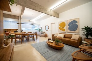 A modern living room with a sofa, coffee table, and chairs, a dining area with a table and chairs, and a kitchen in the background. - Leblon | 3 Quartos, 2 min da Praia - por Casapē Rio (Rio de Janeiro)