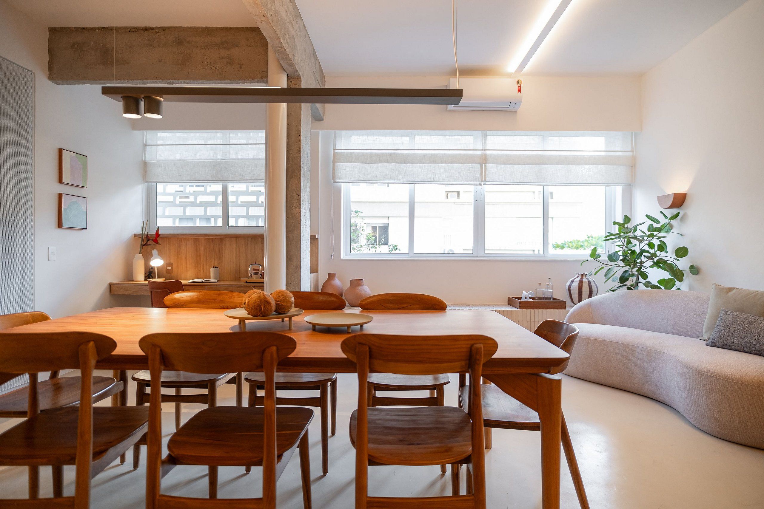 A modern interior with a wooden dining table, chairs, a sofa, and a large window providing natural light.