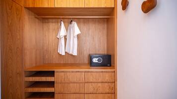 Une armoire en bois avec un coffre-fort noir, deux chemises blanches suspendues et une étagère en bois.