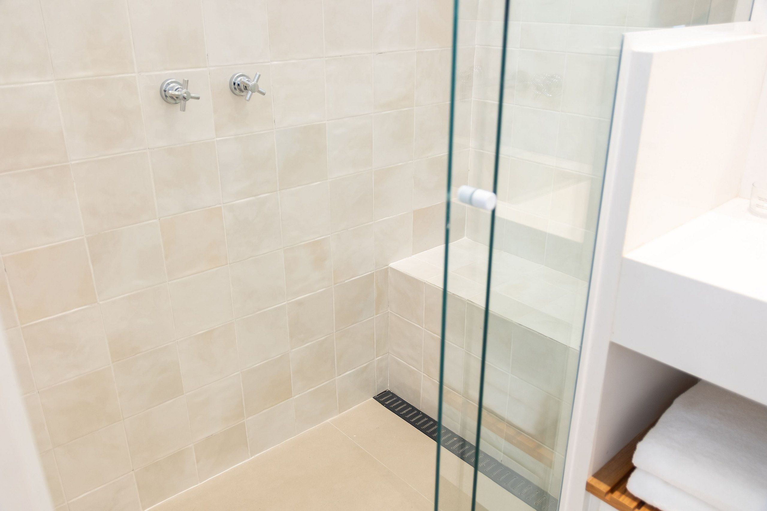 Un baño moderno con azulejos color beige, cabina de ducha con cristal y zona de lavamanos blanca.