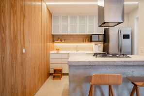 Een moderne keuken met houten kastjes, een beton eiland, roestvrijstalen apparatuur en een klein houten krukje.
