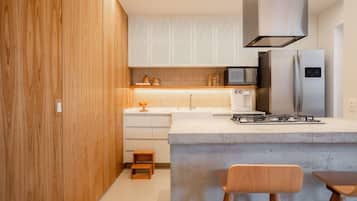 A modern kitchen with wooden cabinets, a concrete island, stainless steel appliances, and a small wooden stool.