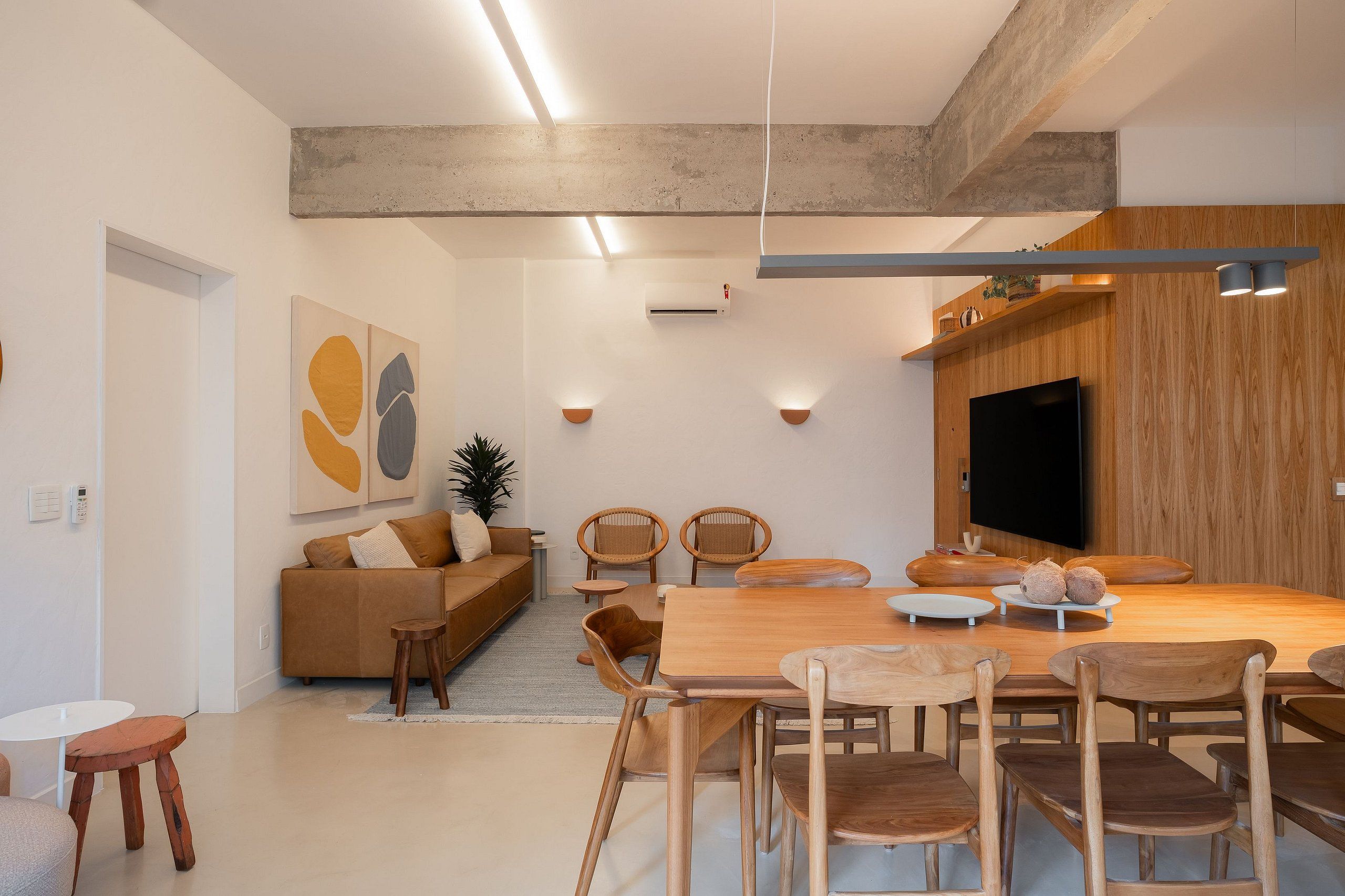A modern living room with a wooden dining table, chairs, a sofa, and a flat-screen TV.