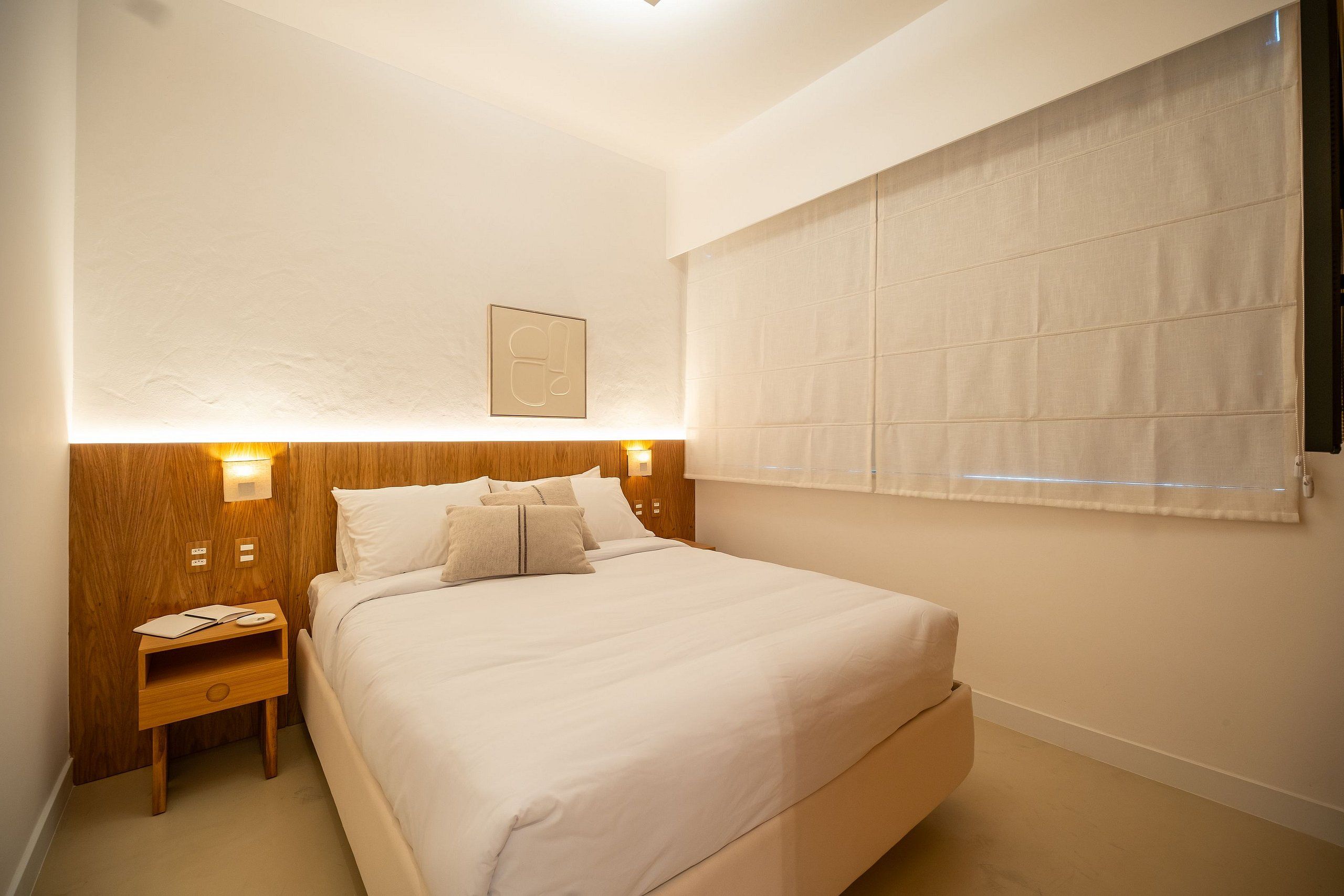 A neatly arranged bedroom with a large bed, bedside tables, and a window with blinds.