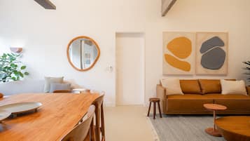 Un salon moderne avec une table à manger en bois, un canapé et des œuvres d’art abstraites accrochées au mur.