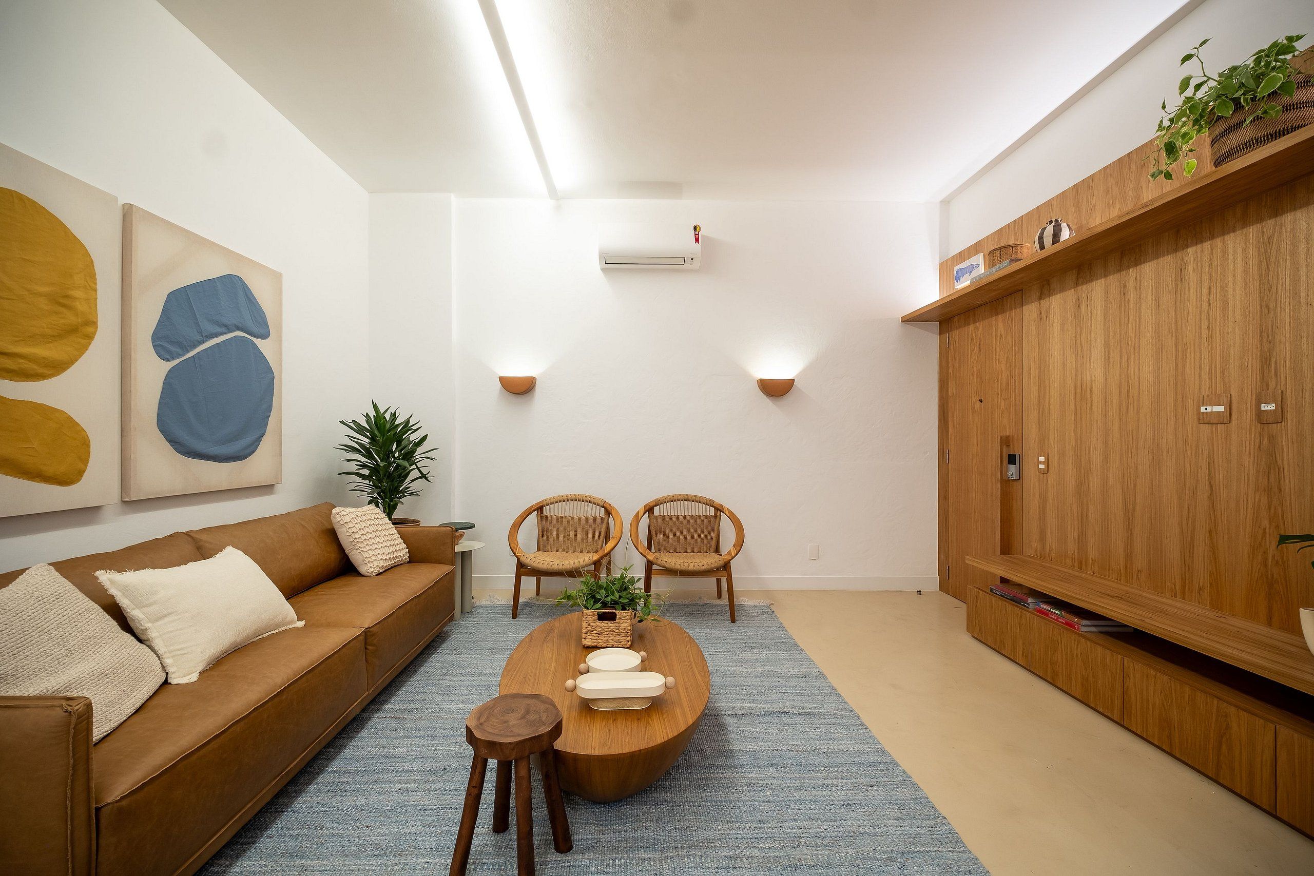 Een moderne woonkamer met een bruine leren bank, twee rieten stoelen, een houten salontafel en een blauw vloerkleed.
