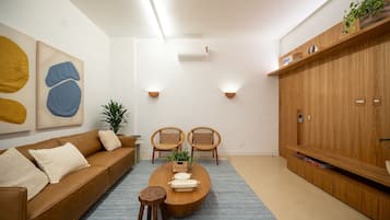Un salon moderne avec un canapé en cuir marron, deux fauteuils en osier, une table basse en bois et un tapis bleu.