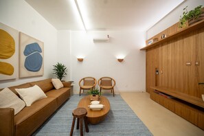 Een moderne woonkamer met een bruine leren bank, twee rieten stoelen, een houten salontafel en een blauw vloerkleed.