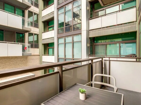 A modern building with multiple floors, large windows, and a balcony area with a table and chairs.