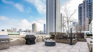 Une terrasse sur le toit équipée d’un barbecue, d’un espace salon et offrant une vue sur les grands immeubles.