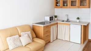 Een kleine keuken met een magnetron, spoelbak en kastje, naast een beige bank met kussens.