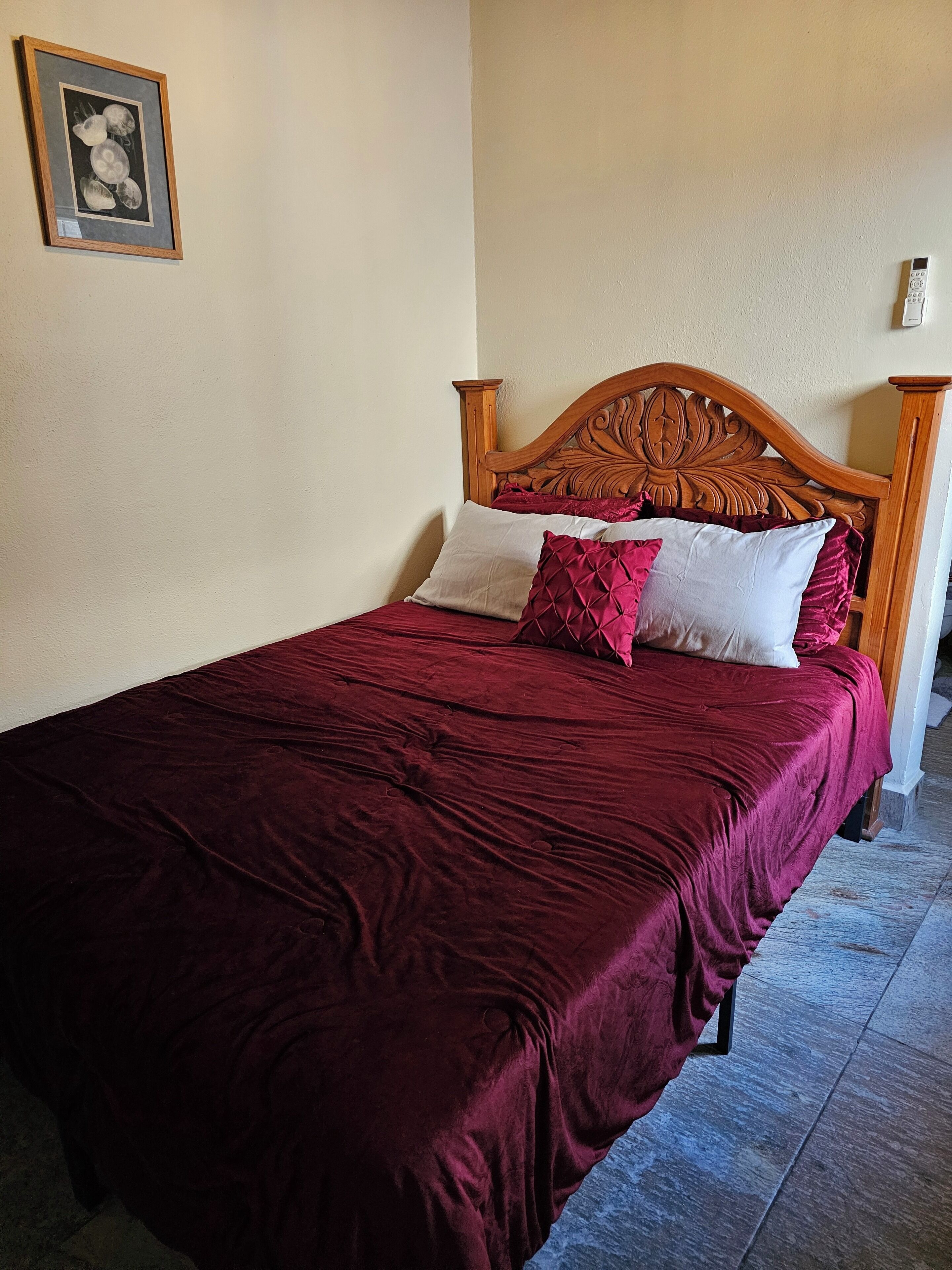 Una cama bien hecha con cabecera de madera, colcha roja y dos almohadas.