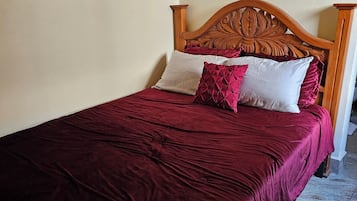 Una cama bien hecha con cabecera de madera, colcha roja y dos almohadas.