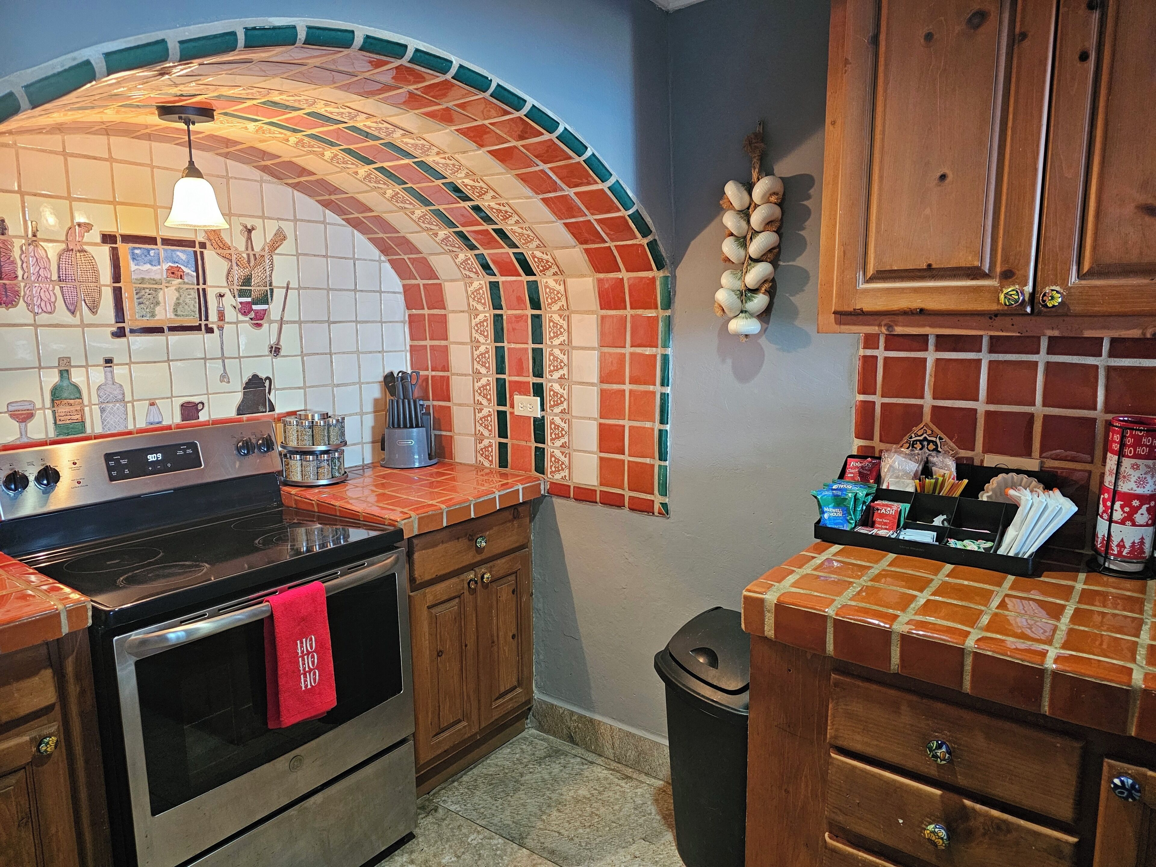 Una cocina con salpicadero de azulejos, armarios de madera, una estufa de acero inoxidable y un cubo de basura.