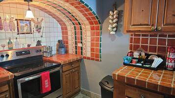 Una cocina con salpicadero de azulejos, armarios de madera, una estufa de acero inoxidable y un cubo de basura.