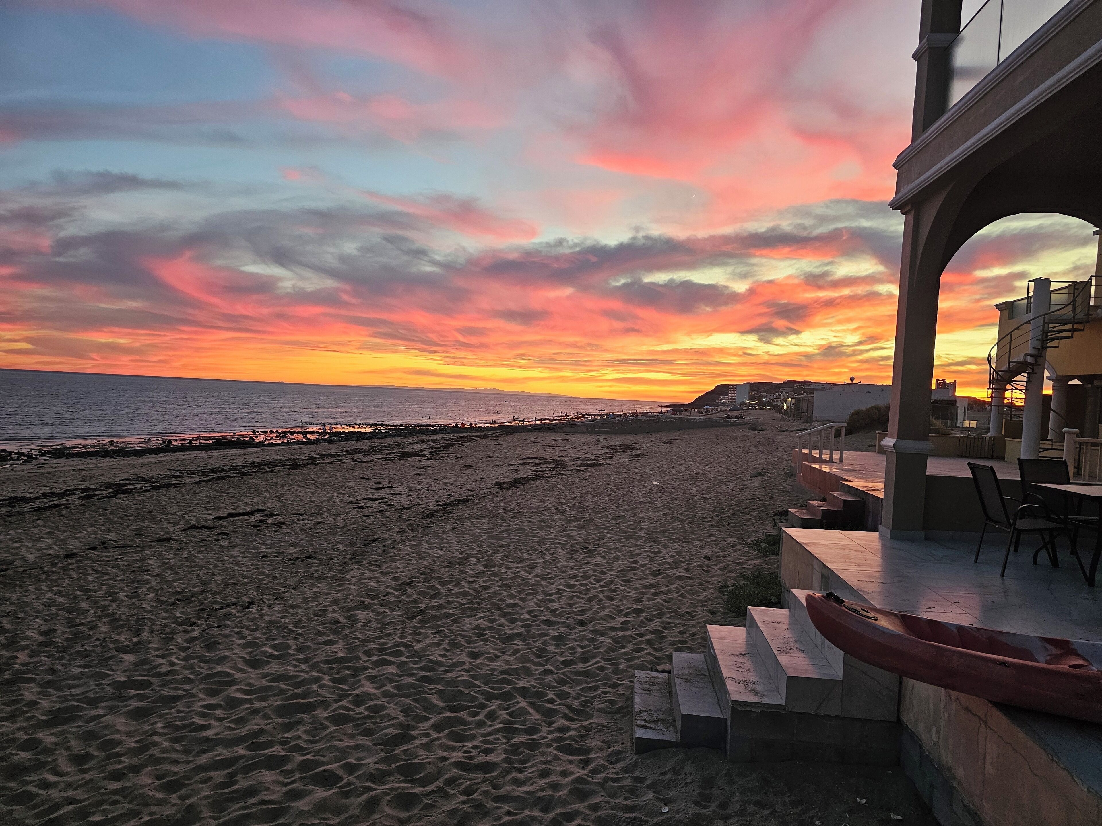 Uma praia com um pôr do sol, um cais e um edifício com área externa para refeições.