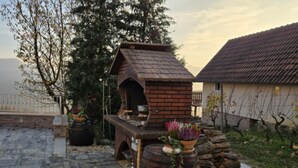 A brick outdoor kitchen with a chimney, a wooden barrel planter with flowers, and a stone stack. - Villa Bella Vista - One Bedroom apartment with Balcony and View (Ivanec)