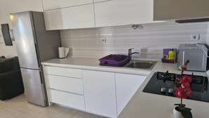 A modern kitchen with white cabinets, a stainless steel refrigerator, a sink with a purple dish rack, and a small stove. - Apartment Slanica Beach Escape - One Bedroom Apartment With Terrace And Sea View (Murter)
